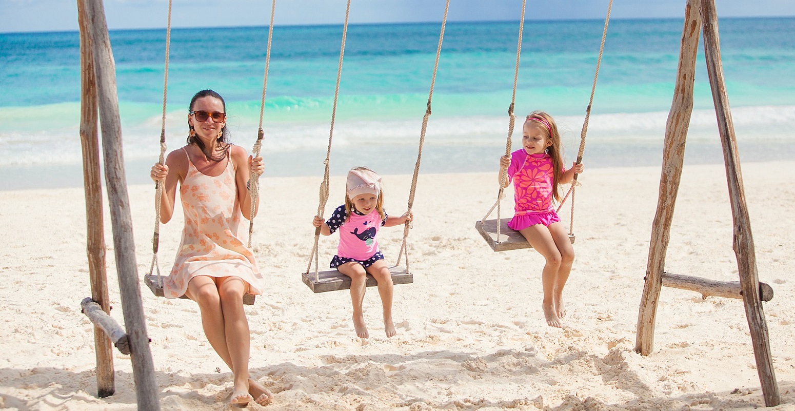 young mother and her cute daughter swinging on a swing at the beach